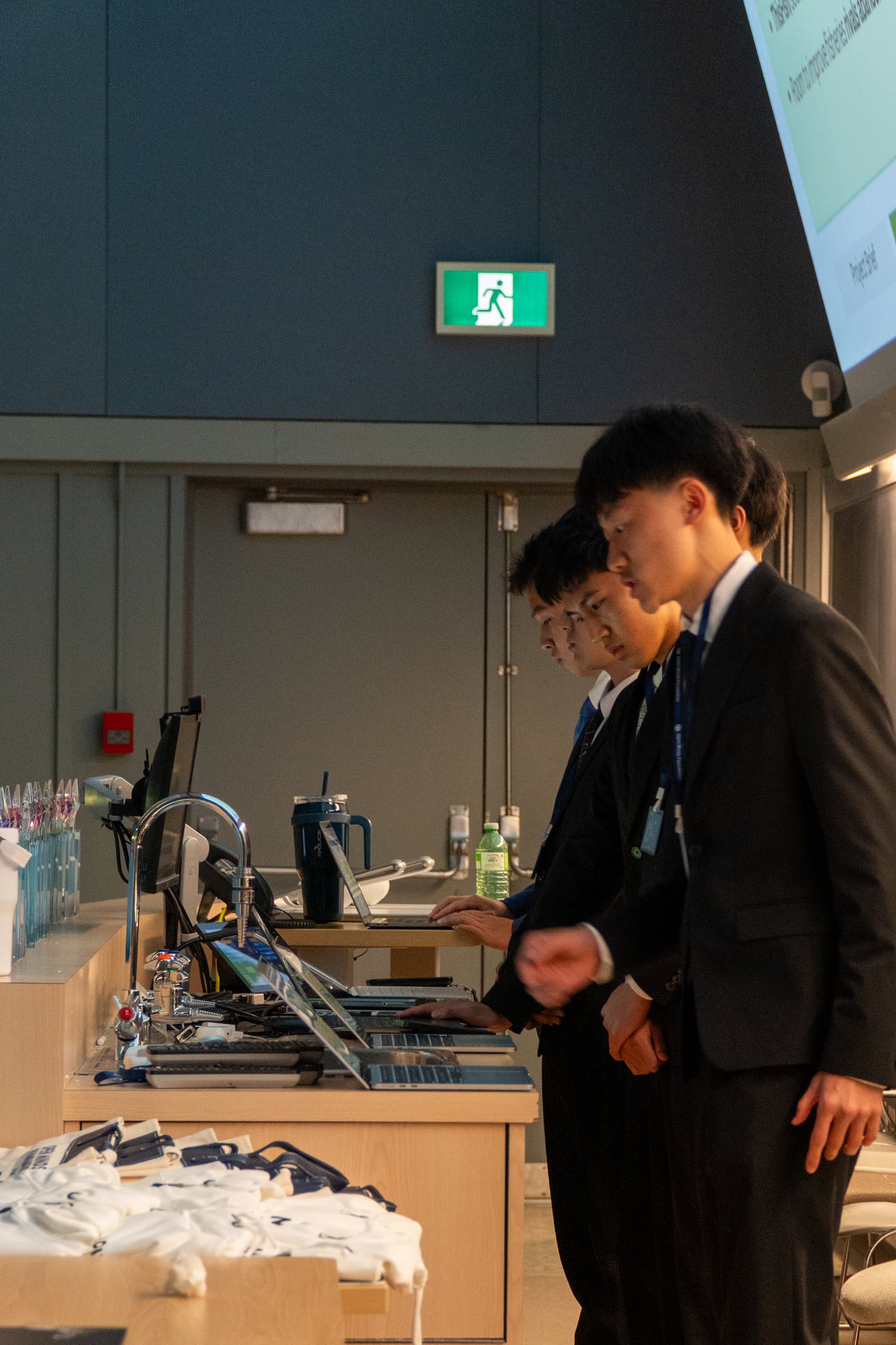 Three students in suits setting up their laptops at the front desk before presenting